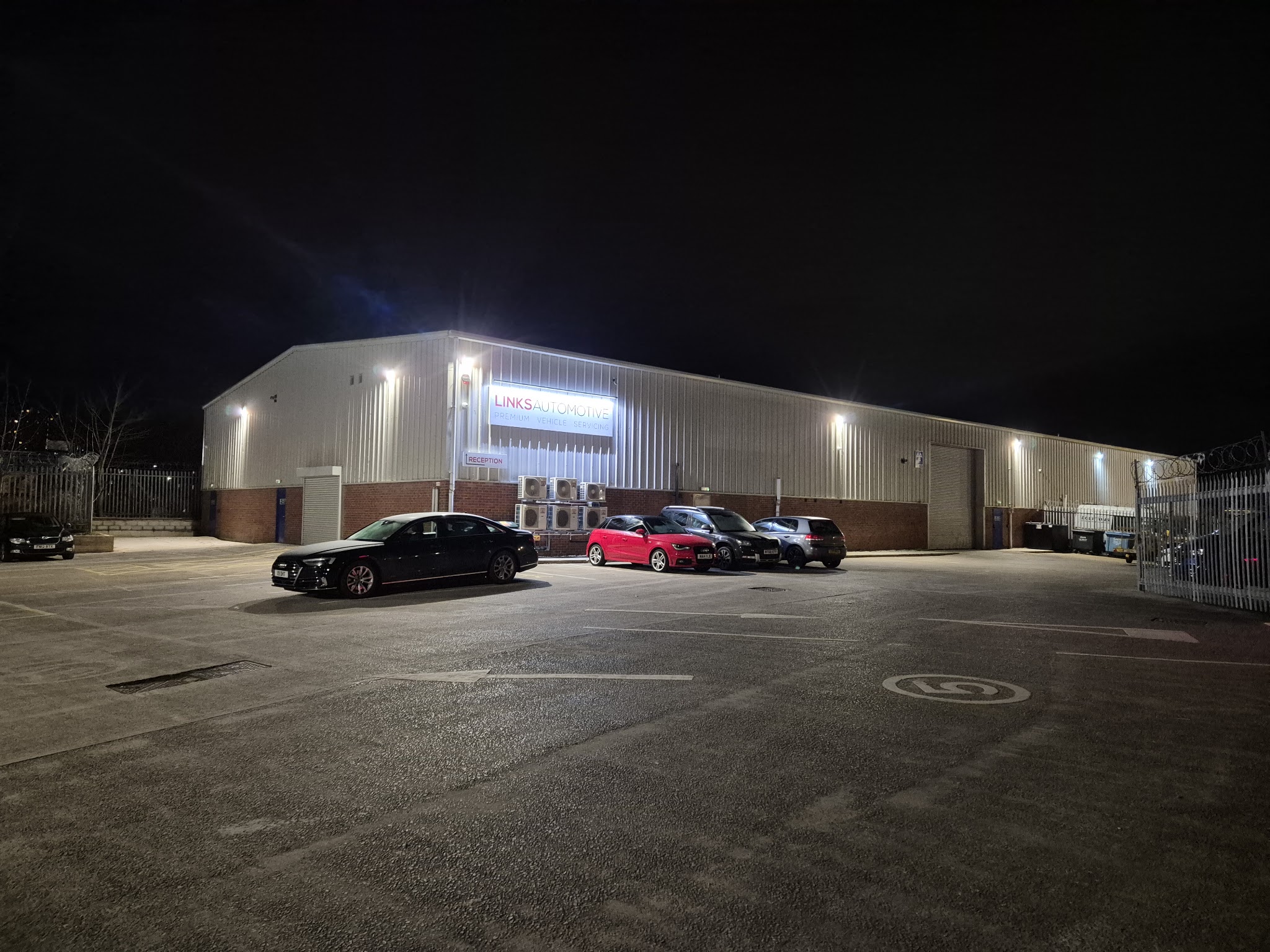 The unit at night, floodlit, with cars parked outside